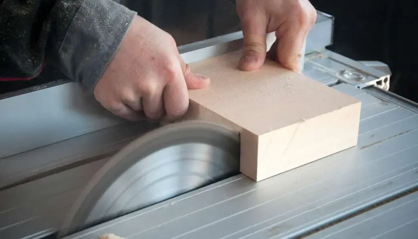 Mani esperte guidano un pezzo di legno su una sega circolare, uno degli attrezzi per tagliare il legno con precisione, per creare un taglio netto.