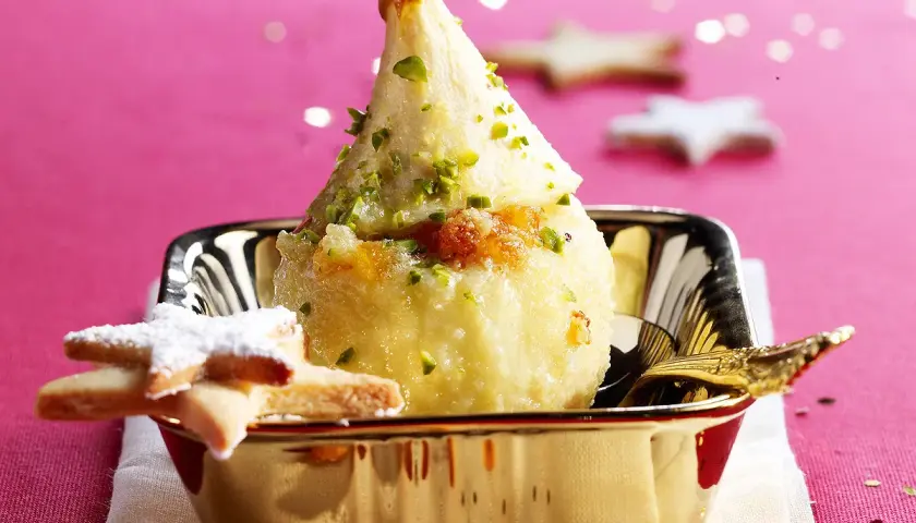 Poire pochée, garnie de pistaches et de miettes de biscuit, servie dans un bol doré. Une idée gourmande pour une recette chartreuse.