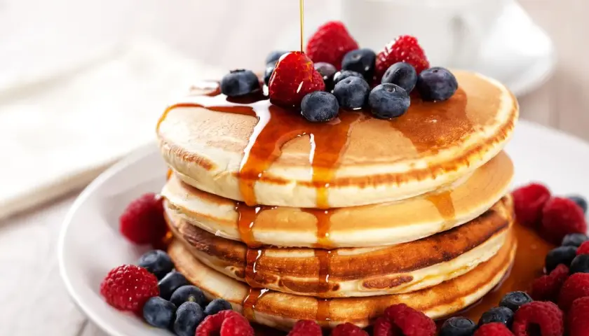 Pancake ricetta: una pila di soffici pancake guarniti con sciroppo d'acero, lamponi e mirtilli freschi.