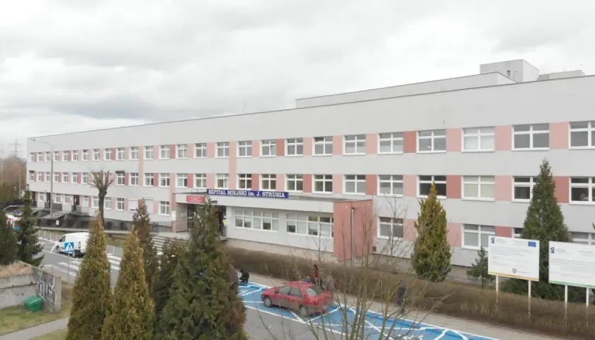 Szpital Miejski im. J. Strusia w Poznaniu. Szukasz informacji, jak dojechać do szpitala na Szwajcarskiej w Poznaniu? Budynek z wieloma oknami, przed którym rosną drzewa.