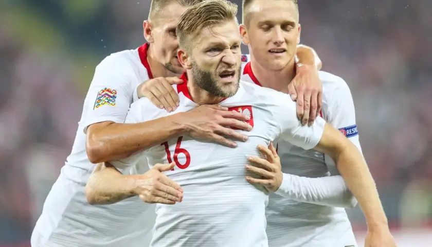 Trzech kapitanów reprezentacji Polski w białych strojach świętuje bramkę.
