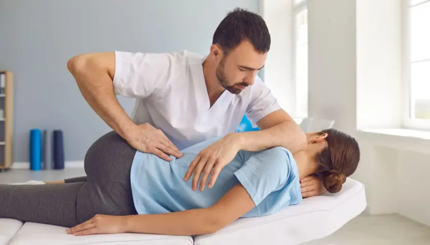Fizjoterapeuta wykonuje terapię manualną kręgosłupa u pacjentki leżącej na kozetce.