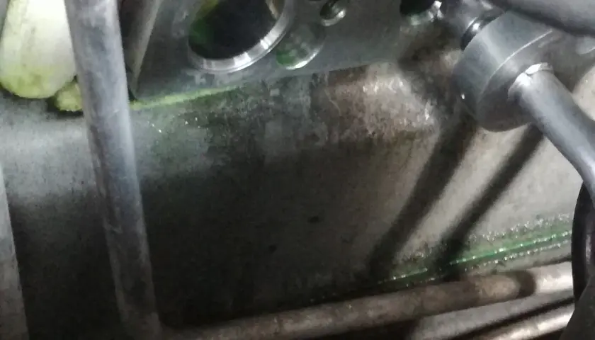 Metalowy blok z otworami, gdzie jest zawór rozprężny klimatyzacji. Widać zielony płyn i rury.