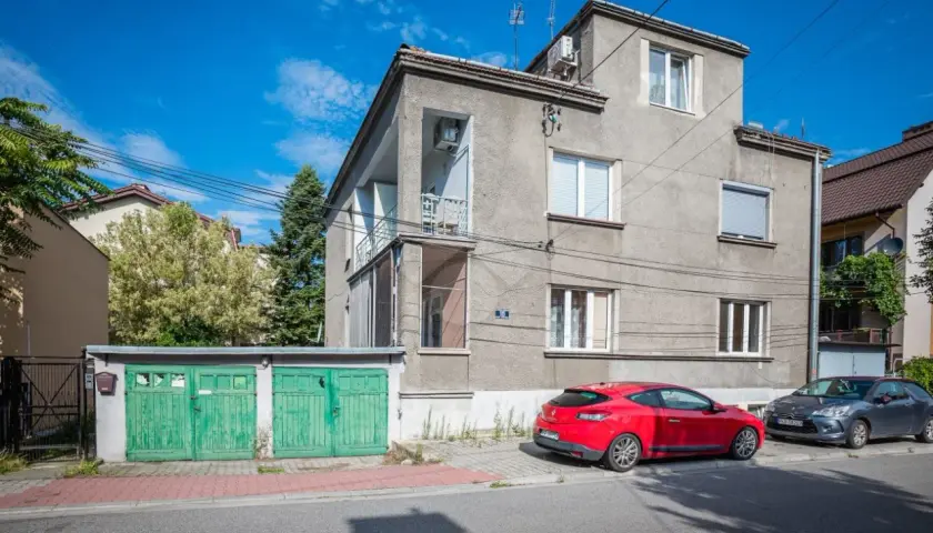 Szare apartamenty Bandtkiego z zielonymi garażami i czerwonym samochodem na tle błękitnego nieba.