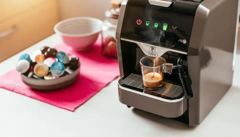 Macchina da caffè prepara un espresso. Accanto, una ciotola piena di capsule colorate, per scegliere se è meglio cialde o capsule.