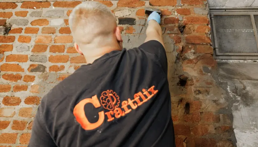 Handwerker mit Handschuh trägt Mörtel auf beschädigtes Mauerwerk auf, um das Injektionsverfahren durchzuführen.