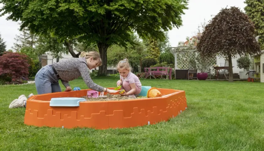 Mama i córka bawią się w piaskownicy na trawniku. Radosne zabawy w piaskownicy w słoneczny dzień.