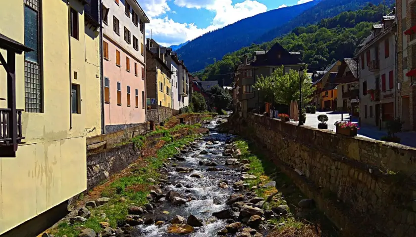 Un río serpentea entre casas de colores y montañas verdes. La **altitud vielha** se siente en el aire fresco y la vista panorámica.