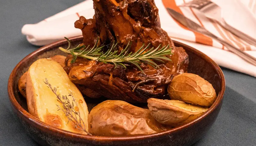Un plat appétissant de souris d'agneau confite, tendre et savoureuse, accompagnée de pommes de terre rôties et d'une touche de romarin frais.