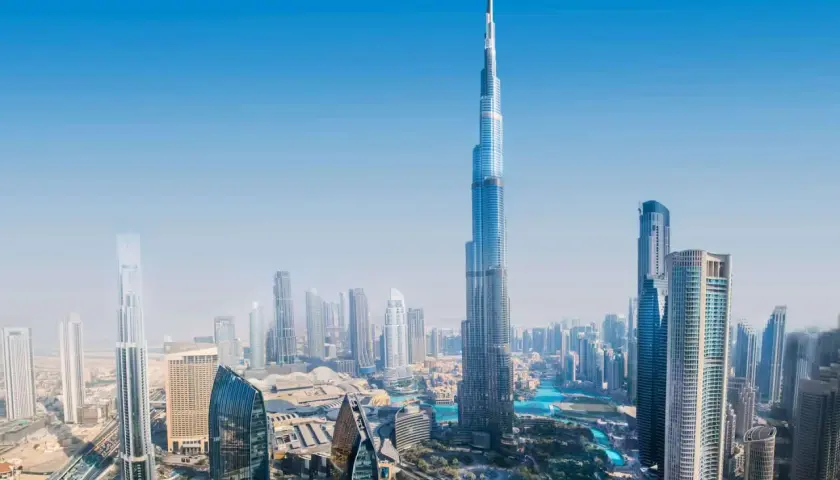 Widok z lotu ptaka na Dubaj, z dominującym Burdż Chalifa. Nowoczesne drapacze chmur i błękitne wody tworzą futurystyczny krajobraz.