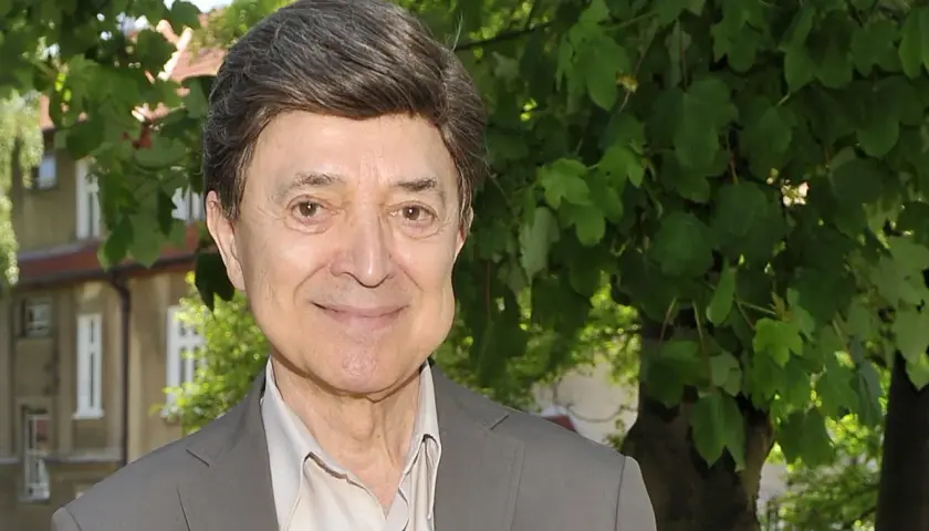 Uśmiechnięty Jerzy Połomski, w szarym garniturze i jasnej koszuli, na tle zieleni. Czyżby szukał partnera do wspólnego śpiewania?