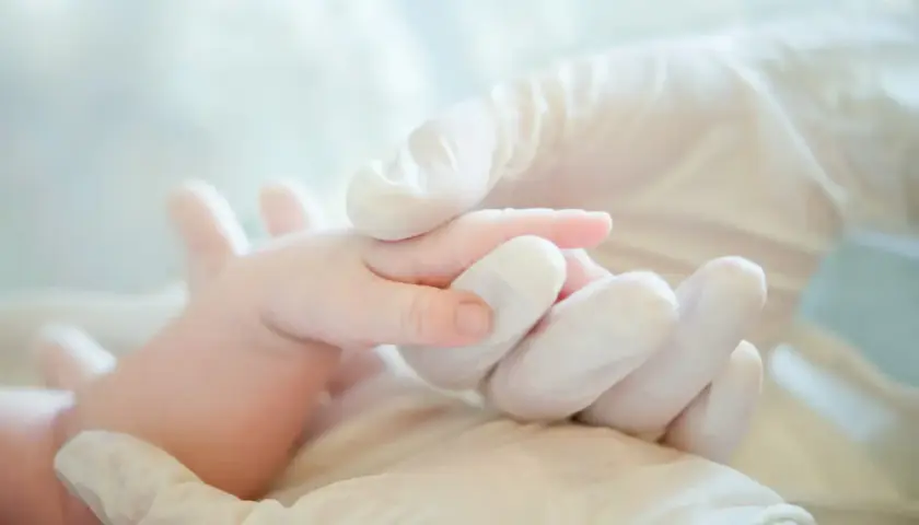 Mani guantate che tengono delicatamente un neonato, un simbolo di cura e attenzione per i possibili danni neurologici da parto.