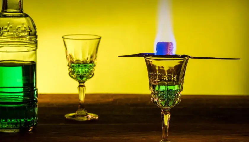 Grüner Absinth brennt über einem Zuckerwürfel in einem Glas. Die Zubereitung lässt die Absinth-Wirkung erahnen.