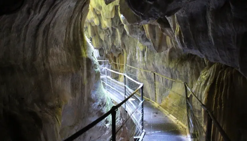 Pasarela metálica serpentea por el interior de los Gorges de la Fou, con paredes rocosas esculpidas por el agua y la luz filtrándose desde arriba.
