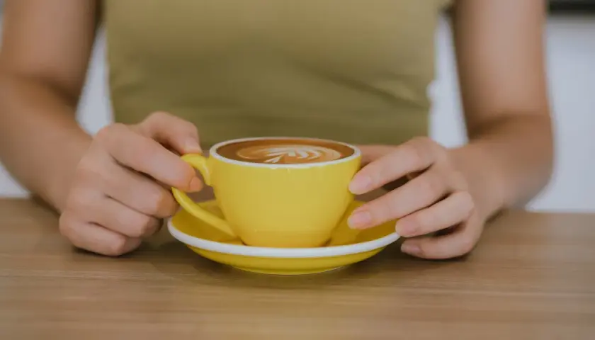 Po treningu zasłużona kawa. Jasnożółta filiżanka z latte art na drewnianym blacie.