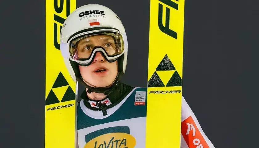 Kacper Tomasiak wzrost – młody skoczek narciarski w kasku i goglach, otoczony żółtymi nartami Fischer.