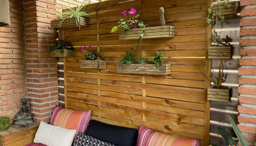 Un rincón acogedor con cojines coloridos y una pared de madera con macetas colgantes, perfecta para tu **diy decoracion** exterior.