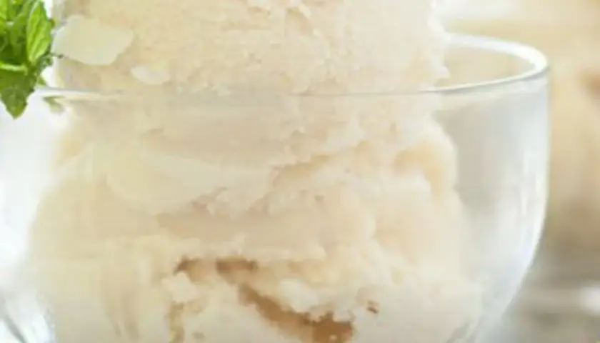 Coppa di gelato alla vaniglia, preparato con panna scremata, guarnita con foglioline di menta fresca.