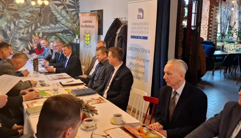 Ludzie siedzący przy stole podczas spotkania, na ścianie baner z logo TUW i napisem "Ubezpieczenia".