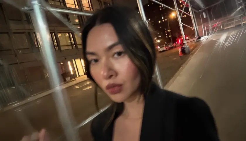 Kvinna med mörkt hår, klädd i svart kavaj, applicerar concealer utomhus på natten.