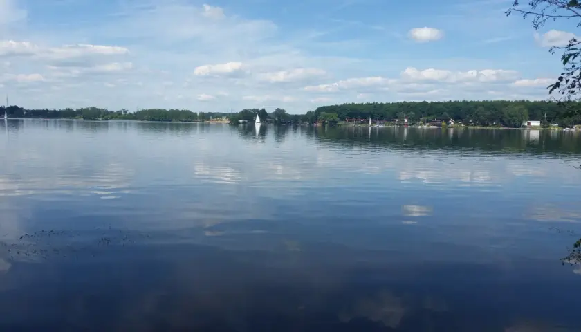 Spokojne **jezioro Pławniowice** z odbijającymi się chmurami i żaglówkami na horyzoncie.