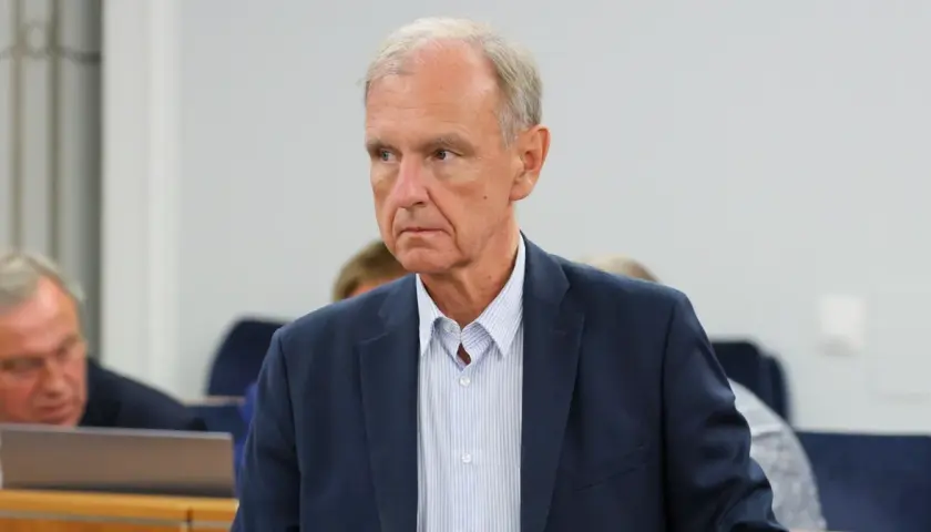 Portret starszego mężczyzny w granatowej marynarce i pasiastym jasnym koszuli.