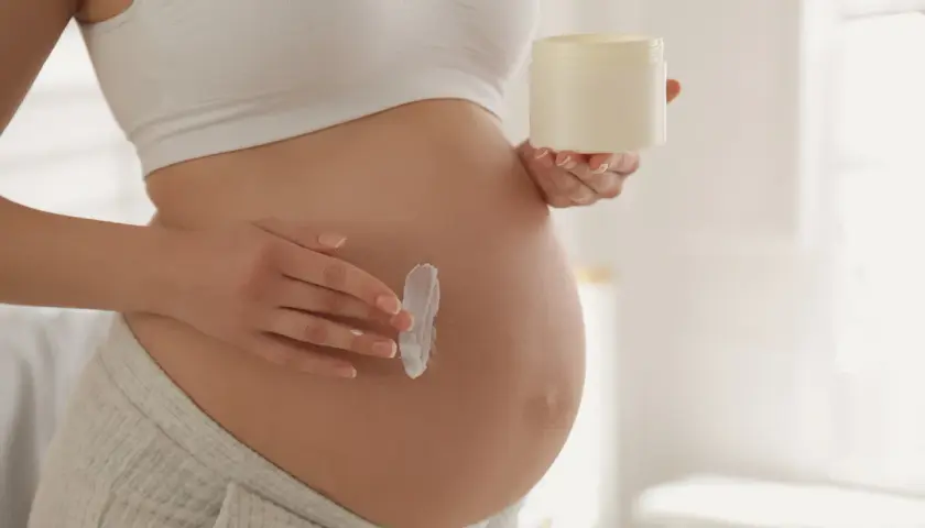 Kobieta w ciąży smaruje brzuch kremem. Delikatna pielęgnacja skóry, jak aloes w ciąży, to ważny element dbania o siebie.