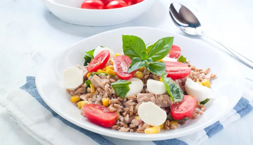 Deliziosa insalata di orzo con tonno, pomodorini, mais e mozzarelline, guarnita con basilico fresco. Un piatto completo e colorato.