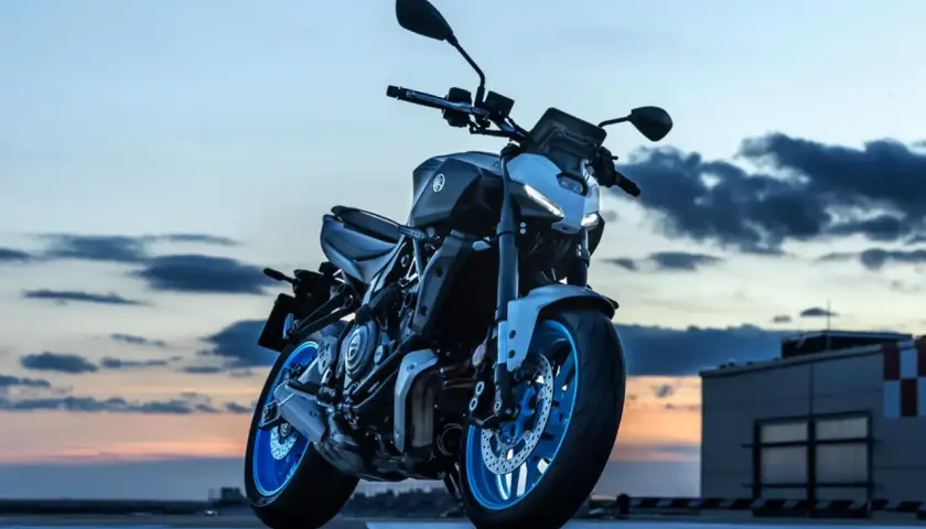 Yamaha MT-07 gotowy do nocnej jazdy. Niebieskie felgi lśnią w blasku zachodzącego słońca.