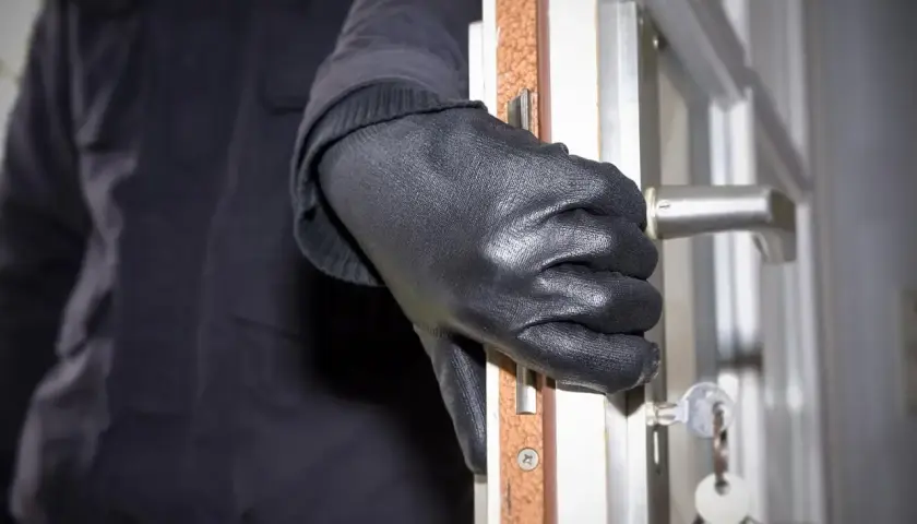 Ręka w czarnej rękawiczce otwiera drzwi, klucze wiszą na zamku. Sen o włamanie może oznaczać niepokój.