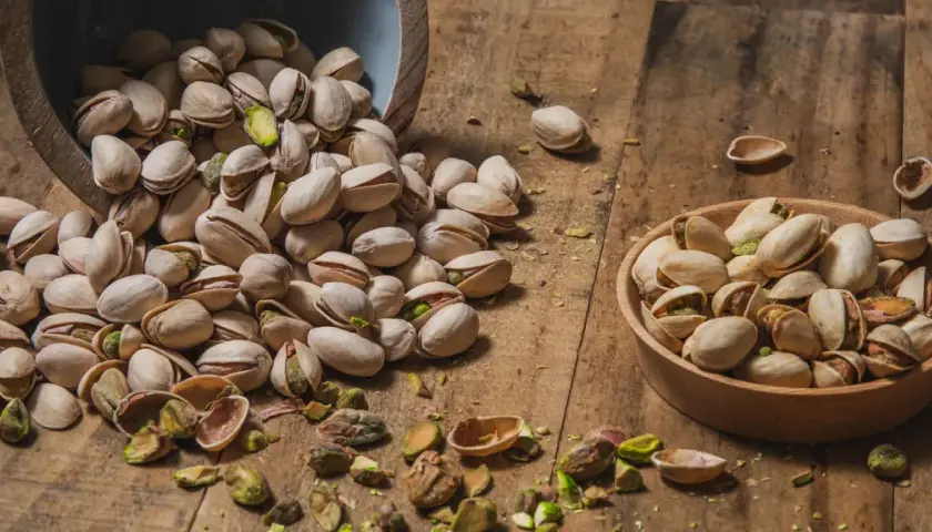 Pistacchi in una ciotola e sparsi su un tavolo di legno. Scopri le incredibili pistacchi proprietà per la tua salute.