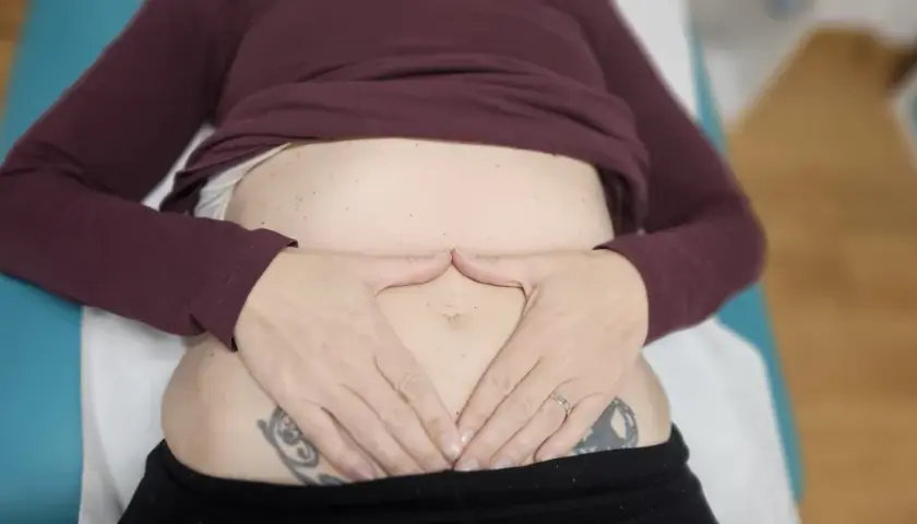 Manos sobre el abdomen, sintiendo el dolor de espalda por gases.