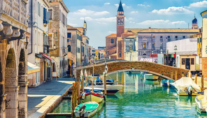 Un rêve d'aller à Venise : un canal bordé de maisons anciennes, un pont de briques et des gondoles.