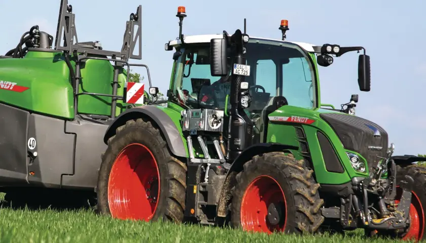 Grüner Fendt-Traktor mit Anhänger auf einem Feld. Die universellen Kabinen für Traktoren bieten Komfort und Sicherheit.