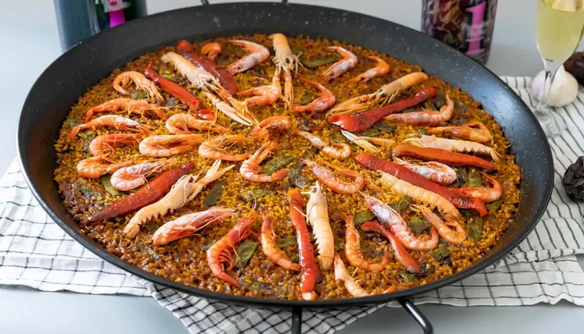 Paella gigante con gambas y pimientos rojos, perfecta para compartir. Cada porción de arroz está llena de sabor.