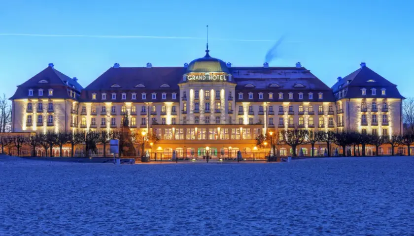 Grand Hotel w Sopocie, jeden z najpiękniejszych hoteli w Polsce, lśni nocą nad piaszczystą plażą.