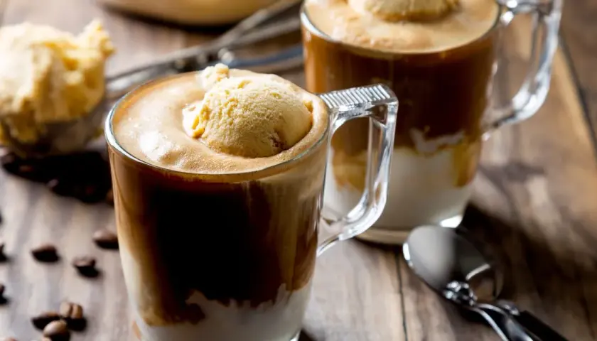 Dwa kubki caffe freddo z gałką lodów waniliowych na wierzchu, na drewnianym stole, obok ziaren kawy.