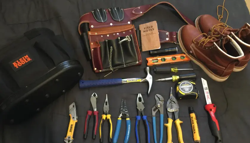 Un cinturón de cuero con múltiples compartimentos, un martillo, alicates, destornilladores, cinta métrica y botas de trabajo. Todo listo para un electricista.