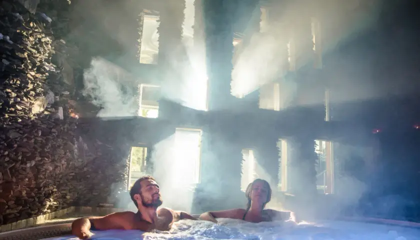 Para spędza relaksujący weekend we dwoje w jacuzzi, otoczona parą i światłem wpadającym przez okna.