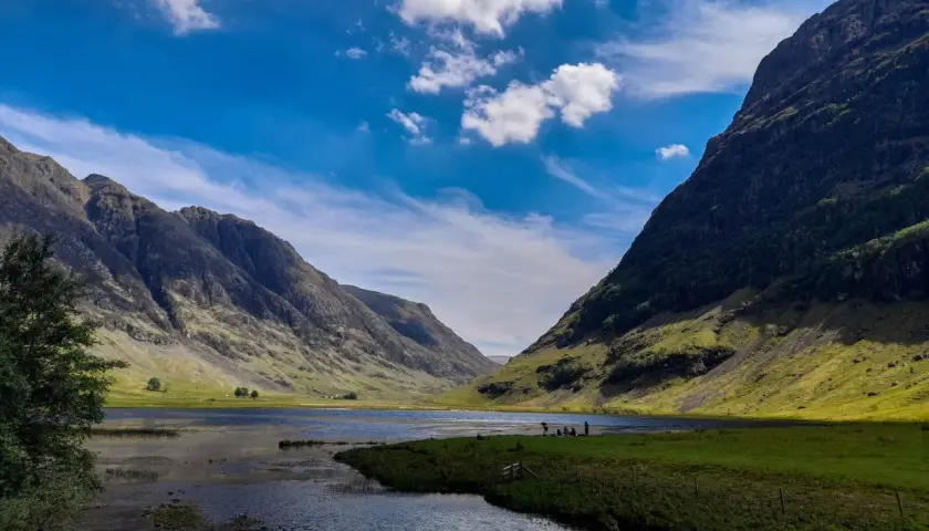 Un paisaje espectacular para hacer **escocia en bicicleta**. Montañas verdes, un lago sereno y un cielo azul con nubes.