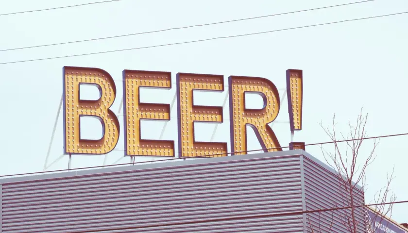 Grand panneau lumineux "BEER!" au-dessus d'un bâtiment moderne. Le nom de bière est écrit en lettres majuscules, illuminées par des ampoules.