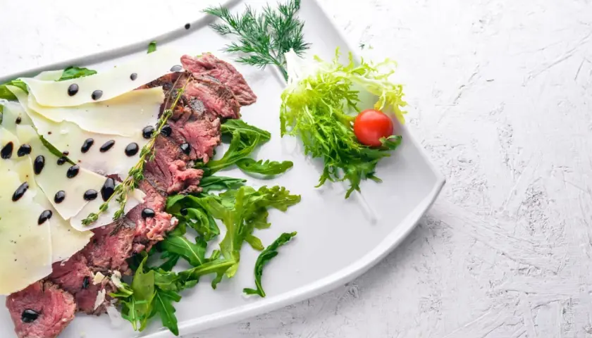 Délicieuse tagliata de boeuf, finement tranchée, garnie de copeaux de parmesan, de roquette fraîche et d'une touche de vinaigre balsamique.