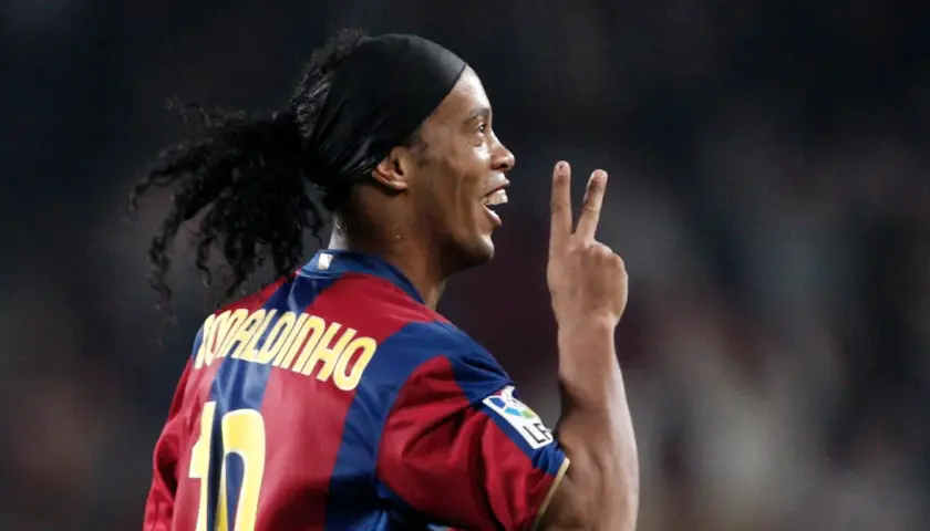 Piłkarz Ronaldinho w koszulce Barcelony, z charakterystyczną opaską na głowie i kucykiem, pokazuje dwa palce. Ile Ronaldinho ma lat?
