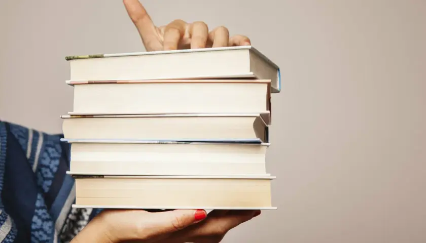 Main tenant une pile de livres, le doigt levé comme pour indiquer un titre. Chaque livre a son propre isbn.
