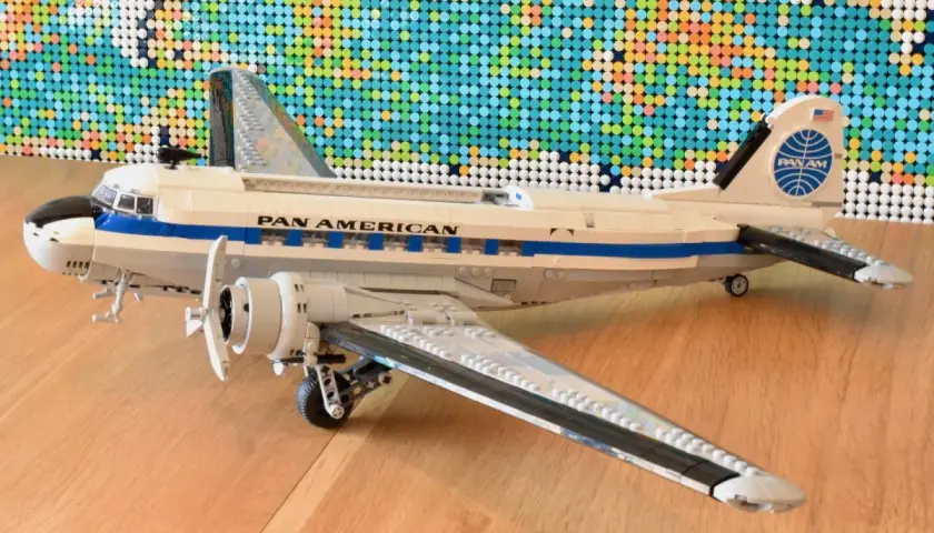 Ein detailreiches Lego DC-3 Flugzeug der Pan Am steht auf einem Holzboden, im Hintergrund eine bunte Lego-Weltkarte.