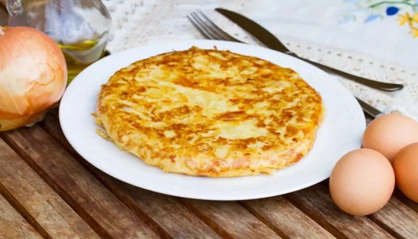Frittata di patate dorata su piatto bianco, con cipolla, uova e olio d'oliva come ingredienti.