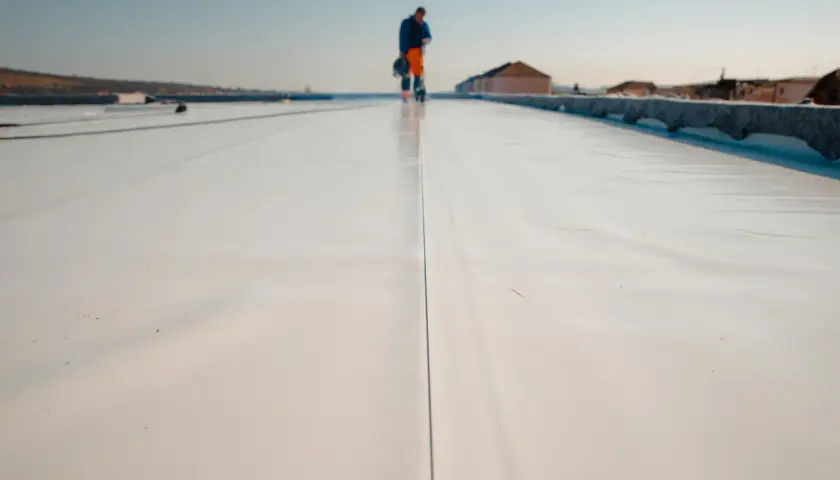 Arbeiter auf einem hellen Flachdach, das für die Windsogsicherung vorbereitet wird.