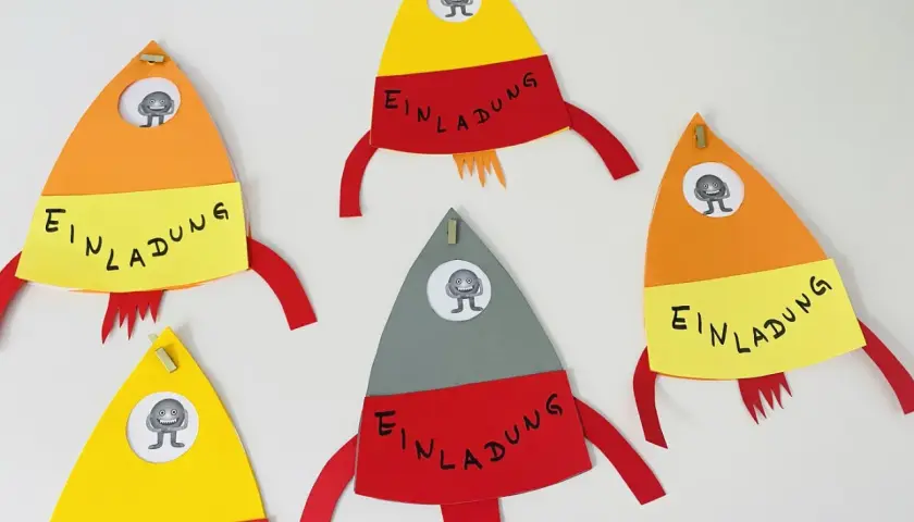Bunte Raketen zum raketen einladung basteln, jede mit einem kleinen Monster im Fenster und dem Wort "Einladung" auf gelbem Band.