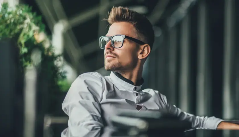 Florian, młody mężczyzna w okularach, w białej koszuli, spogląda w bok, zamyślony.