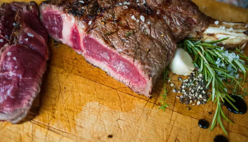 Une belle côte de bœuf de 1,2 kg, parfaitement saisie, prête pour la cuisson. Sel, poivre, ail et romarin accompagnent cette pièce de viande juteuse.